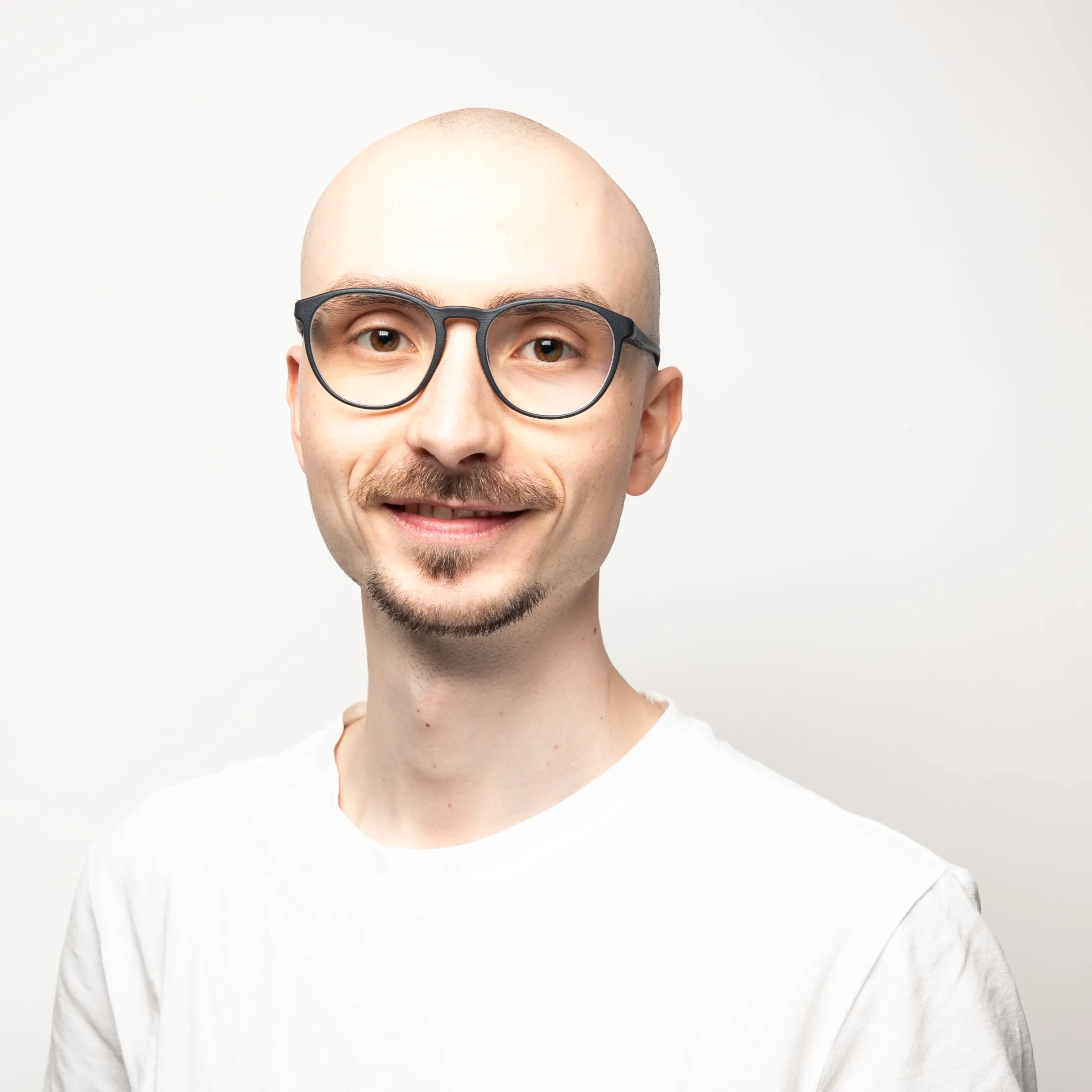 A bald man with a beard. He is wearing blue glasses, looking directly into the camera, and smiling. It is a portrait shot.